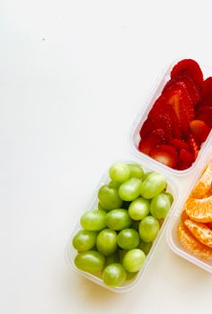 Top view of sliced strawberries, grapes, and oranges in containers, perfect for a healthy snack.