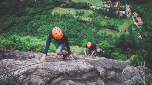 Free Three climbers ascend a rocky cliff with lush green rice fields in the background. Stock Photo