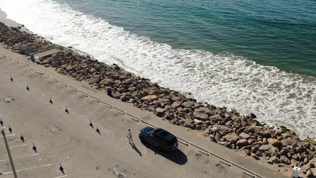 Aerial view of a car parked by the ocean with rocky shore and waves in Malibu, California.