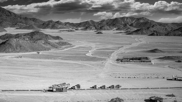 A dramatic black and white desert scene with safari vehicles and mountains under a striking sky.