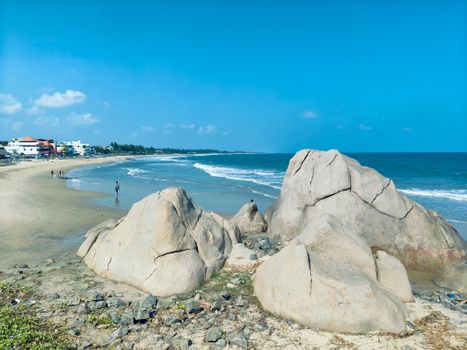 Relaxing seaside view with large rocks, sandy beach, and vibrant blue ocean under clear skies.