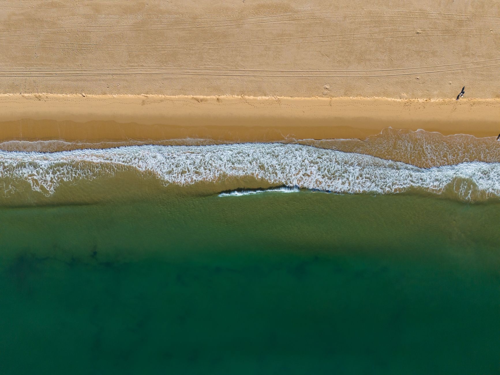 Stunning aerial view of Praia de São Roque beach with turquoise waves and golden sand in Lagos, Portugal.