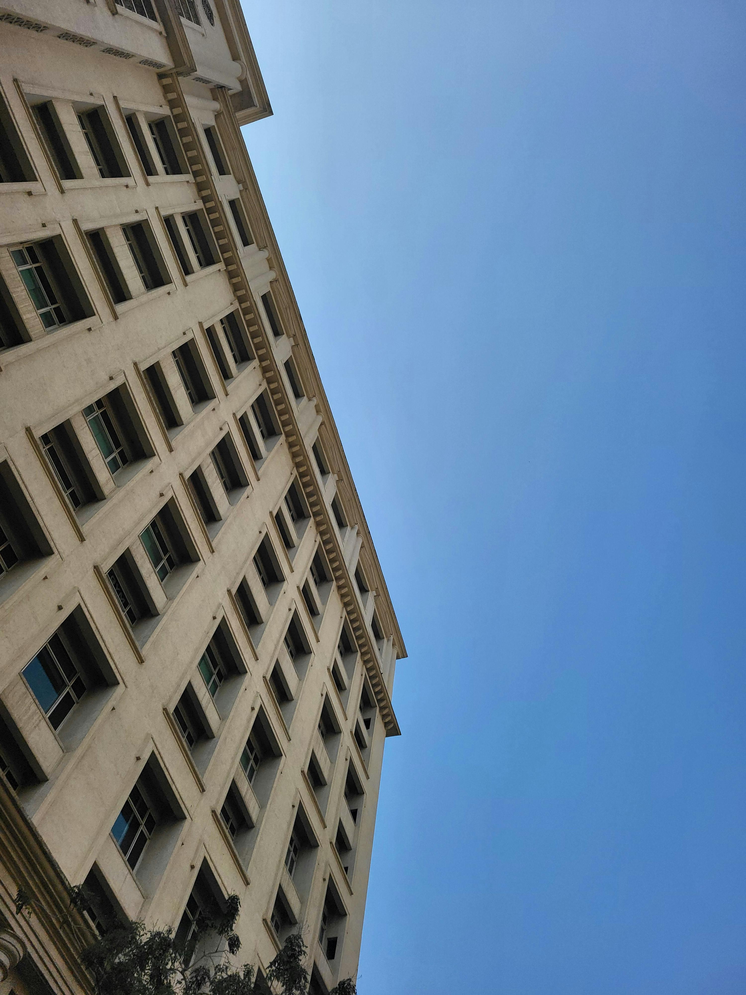 Zadarmo Pohľad z nízkeho uhla na vysokú budovu s klasickými architektonickými detailmi pod jasnou modrou oblohou. Fotka z fotobanky