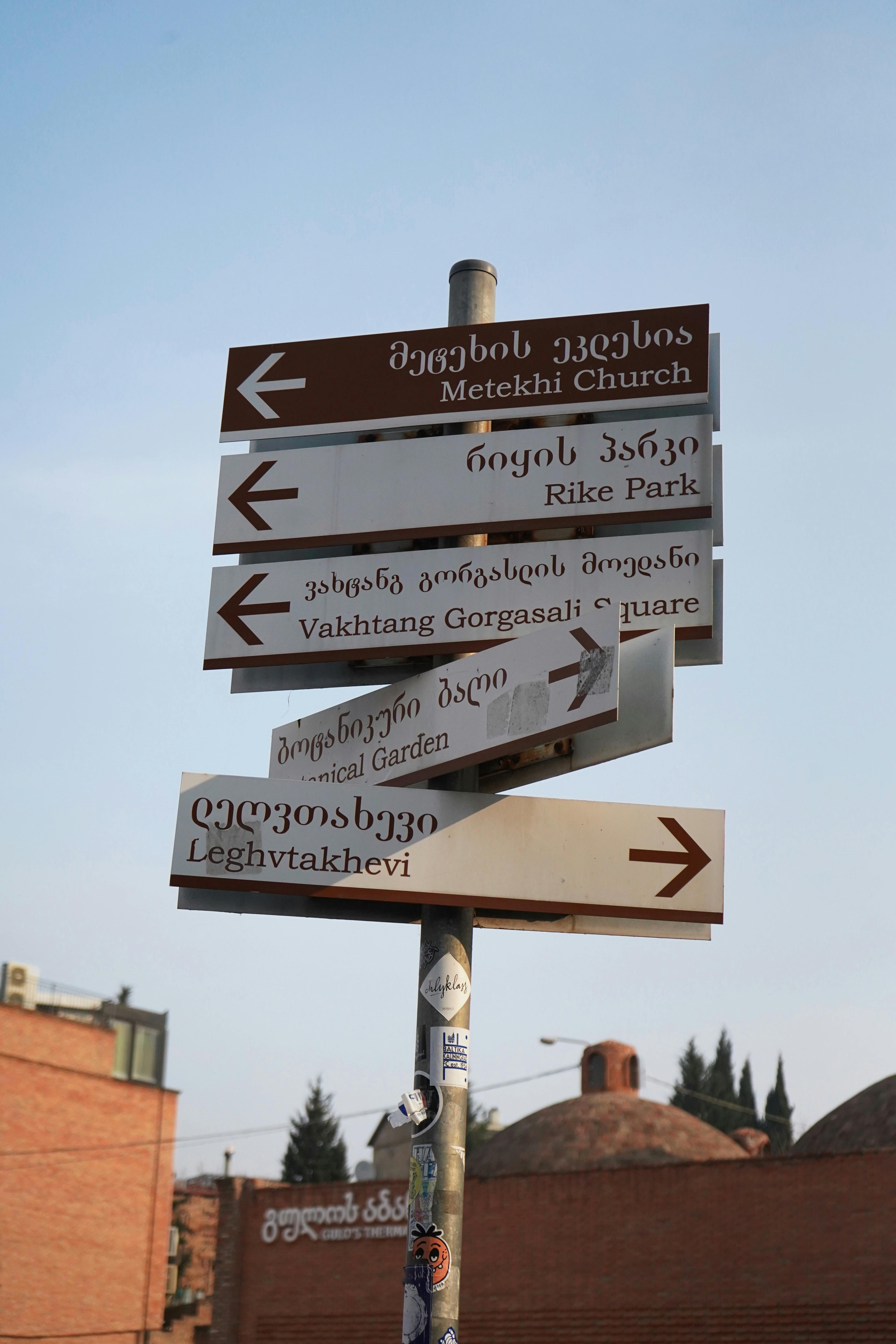 A directional signpost pointing to landmarks in Tbilisi, Georgia, against a blue sky.