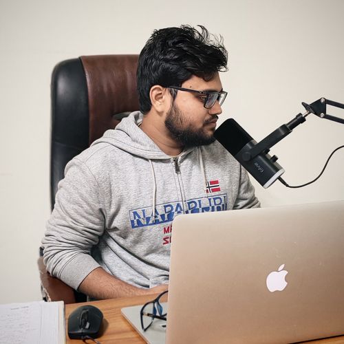 Free A young man in casual wear recording a podcast at his home office desk with a laptop and microphone. Stock Photo