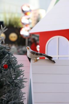 Decorative bird perched atop a snow-covered rooftop next to a festive Christmas tree.