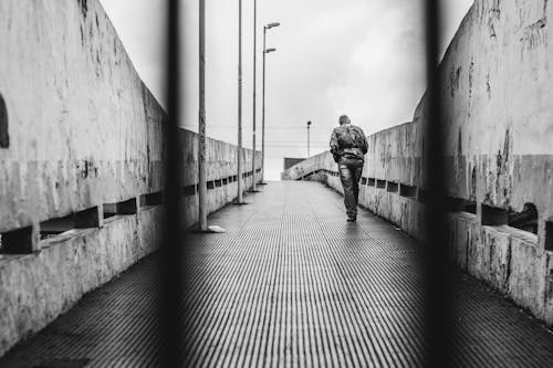 бесплатная Фотография человека в куртке и штанах, идущего по тротуару в оттенках серого Стоковое фото