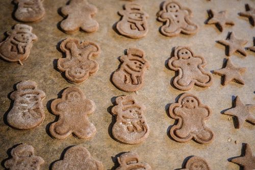 Free A batch of uncooked gingerbread cookies shaped like snowmen and stars on parchment paper. Stock Photo