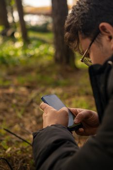 A young adult explores the outdoors using a smartphone amidst greenery in a forest.