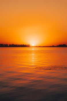 Tranquil sunset scene with vivid orange skies over a peaceful lagoon, ideal for serene and calming nature themes.