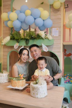 Smiling parents and child celebrating birthday with cakes and balloons indoors.