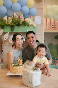 Joyful family celebrating their toddler's birthday with cake and balloons indoors.