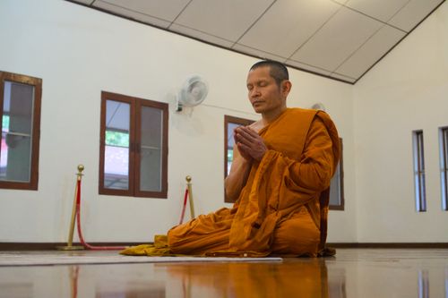 Free A monk in orange robes meditates inside a serene Chiang Mai temple, embodying peace and spirituality. Stock Photo