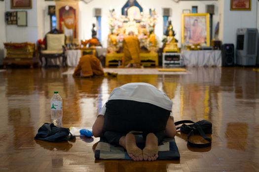 A person kneeling in prayer inside a Buddhist temple in Chiang Mai, Thailand.