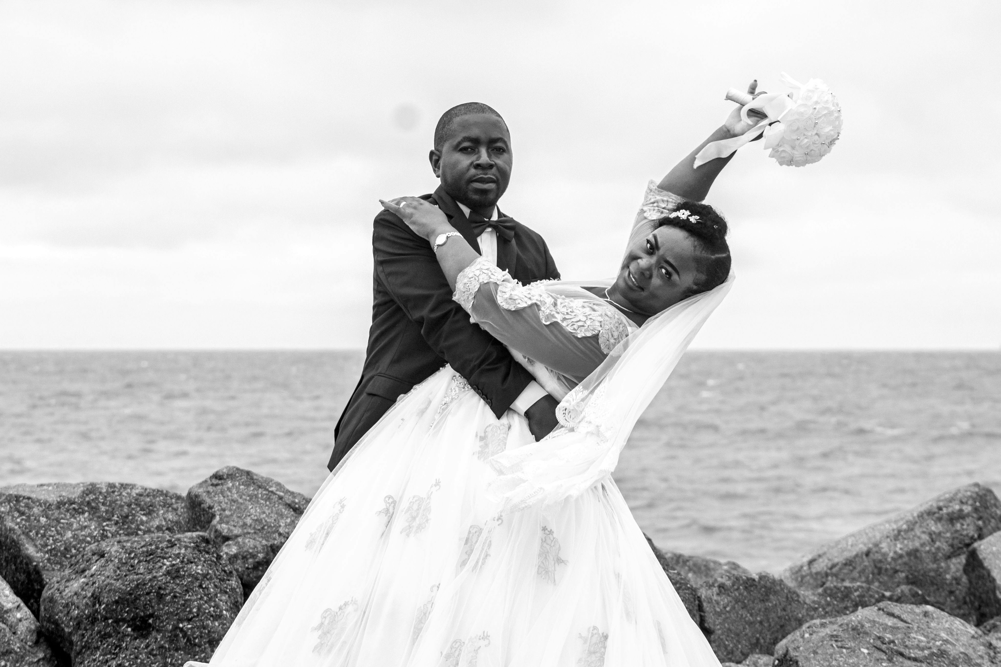 Black and white photo of a joyful couple on their wedding day by the seaside.