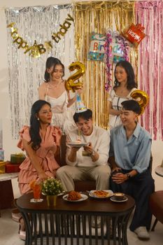 A group of friends celebrating a birthday indoors with cake and decorations in Jakarta.