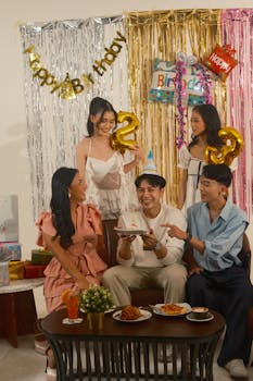 Group of young adults celebrating a birthday party indoors with decorations and cake.
