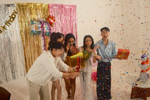 Group of friends celebrating a birthday indoors with gifts, decorations, and confetti.