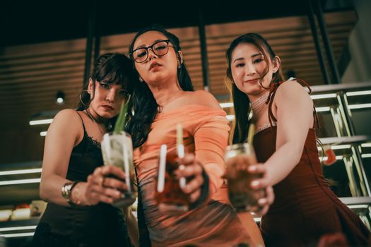 Three stylish women in evening dresses enjoying cocktails indoors, capturing the spirit of celebration.