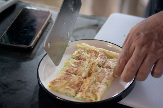 A chef slices freshly cooked flatbread on a plate in a kitchen setting.