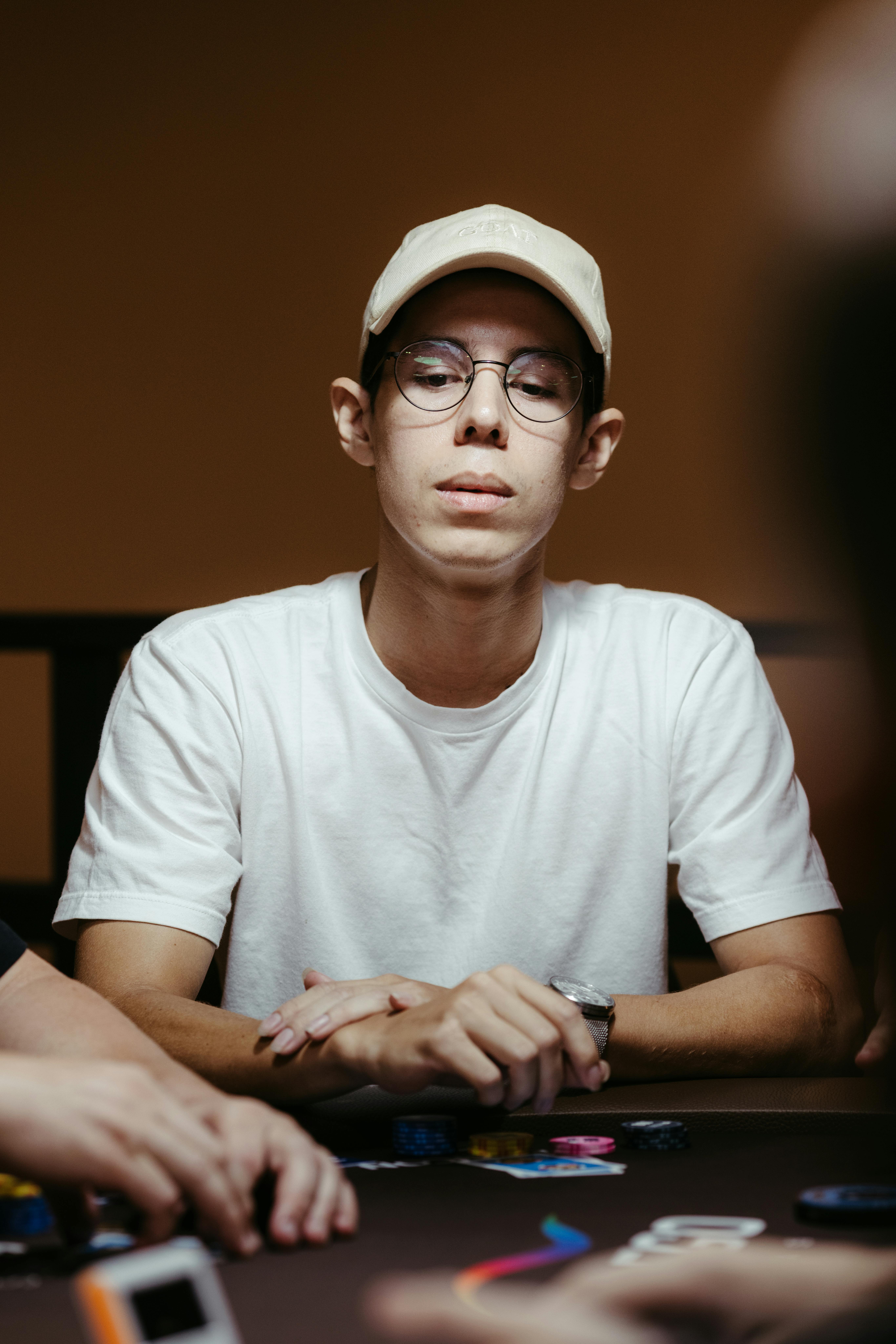 Young man playing poker indoors, concentrating on his gameplay. Cards and chips visible on the table.