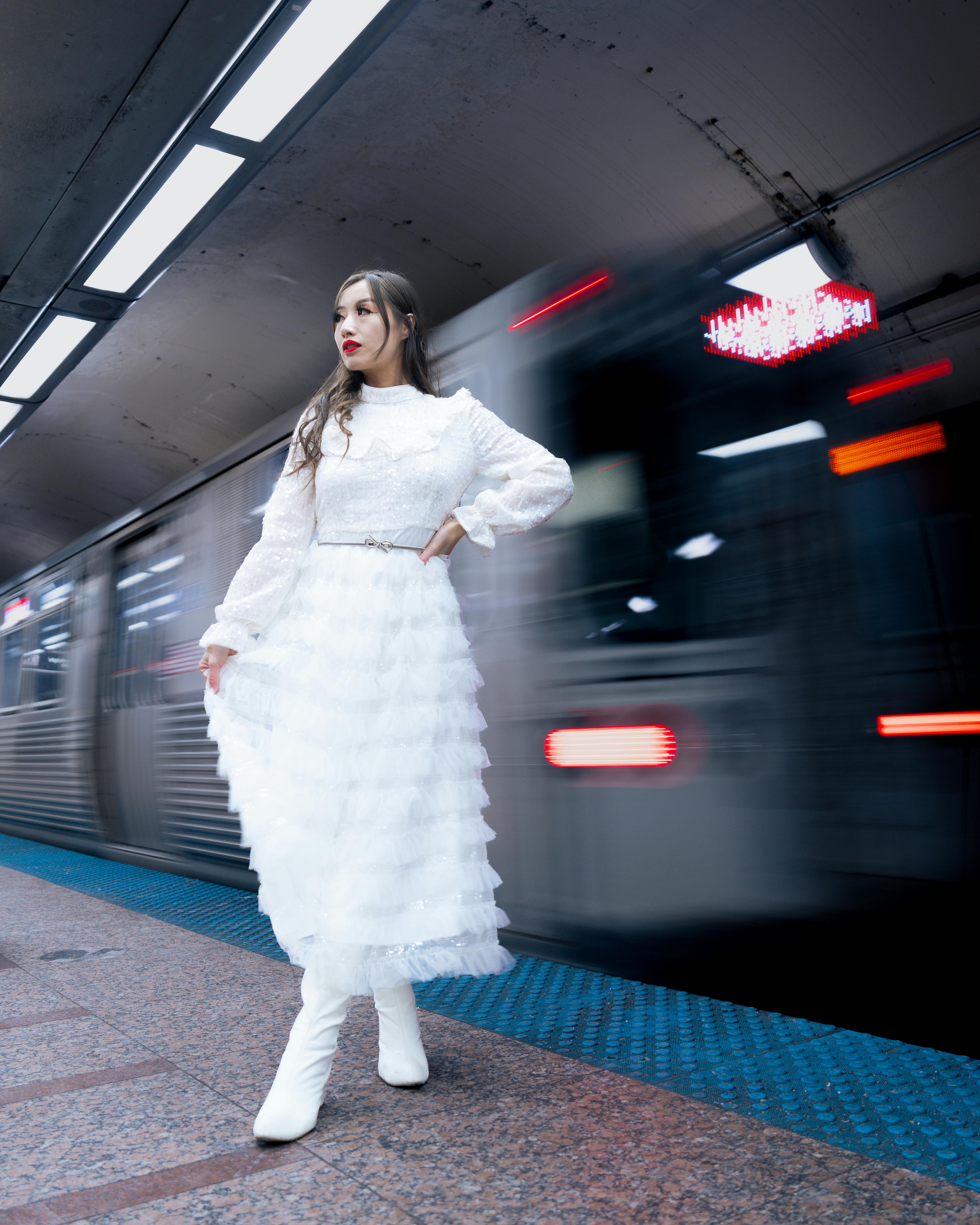 Stylish woman in white dress posing in a subway station. Motion blur of passing train adds drama.