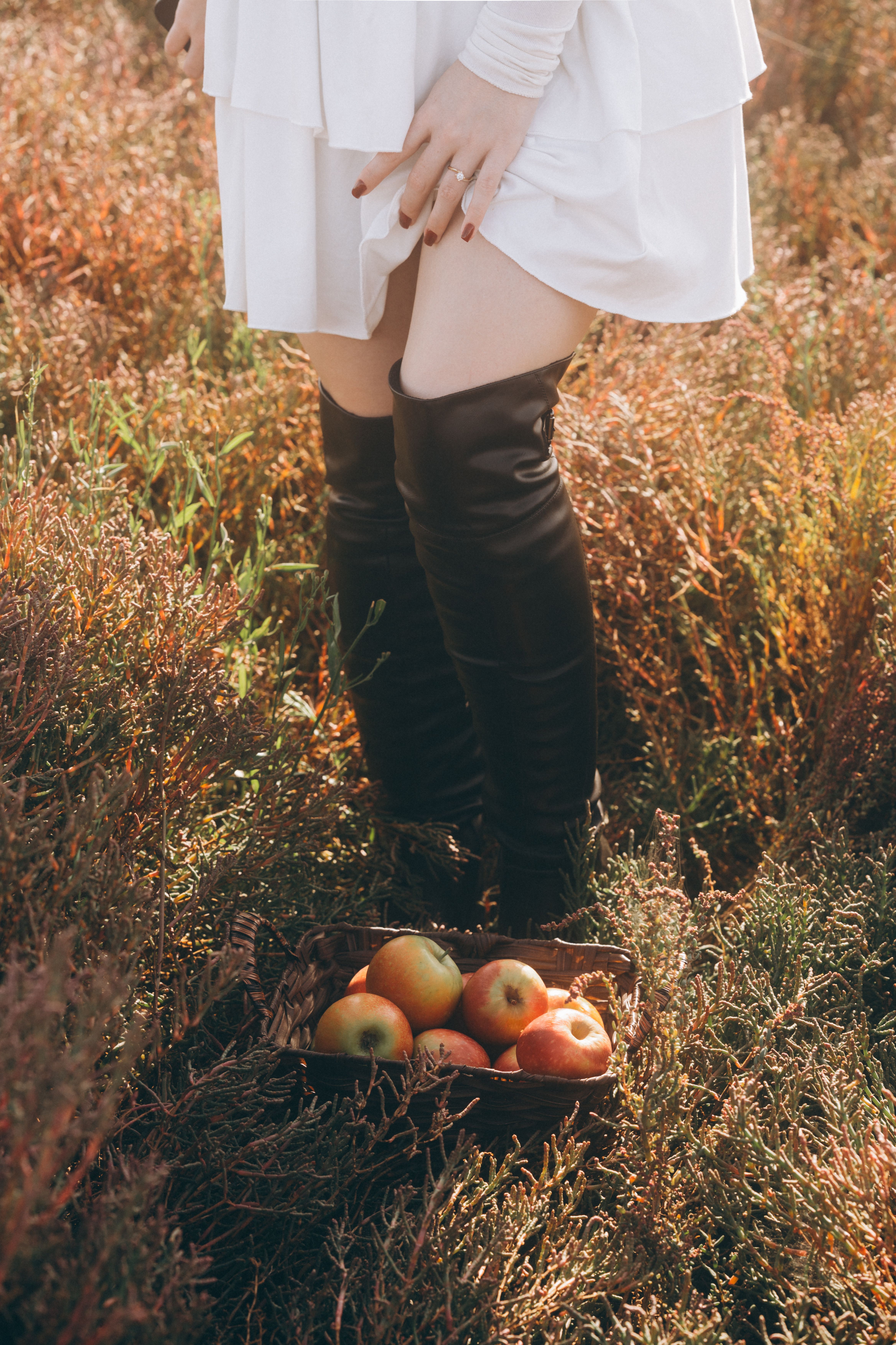 Fashionable woman in autumn field with basket of apples, capturing seasonal charm.