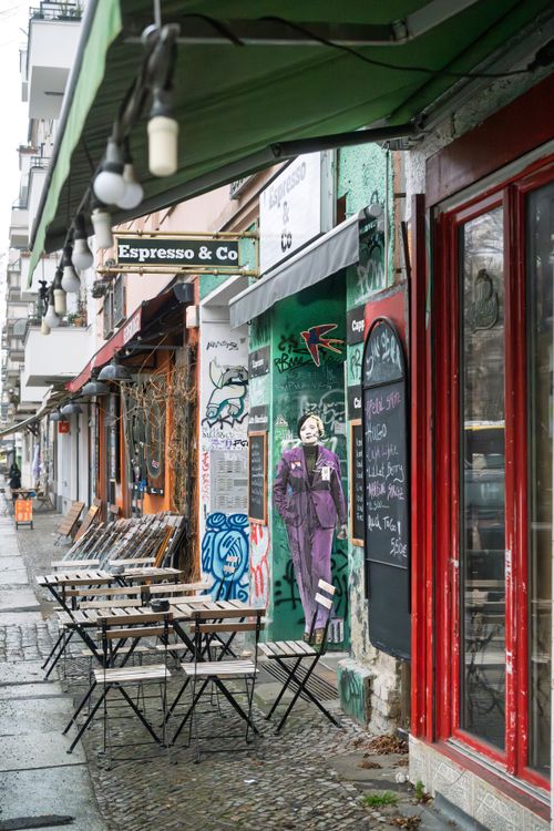 Free Chic Berlin cafe street with outdoor seating, notable for its graffiti art and urban ambiance. Stock Photo