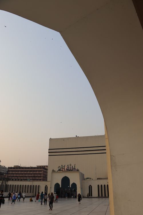 Free A mosque archway silhouetted against an evening sky with visitors entering the building. Stock Photo