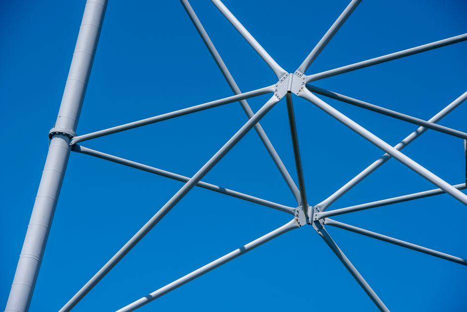 A detailed view of a modern steel mast structure set against a clear blue sky, showcasing engineering elements.