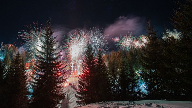 Captivating fireworks illuminate the night sky above a snowy forest, creating a magical winter spectacle.