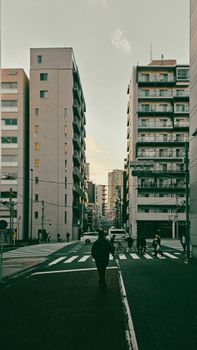 City street view featuring pedestrians crossing at twilight in a modern urban setting with tall buildings.