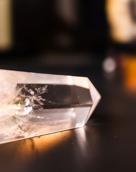 A detailed close-up of a clear quartz crystal resting on a dark surface with soft focus light reflections.