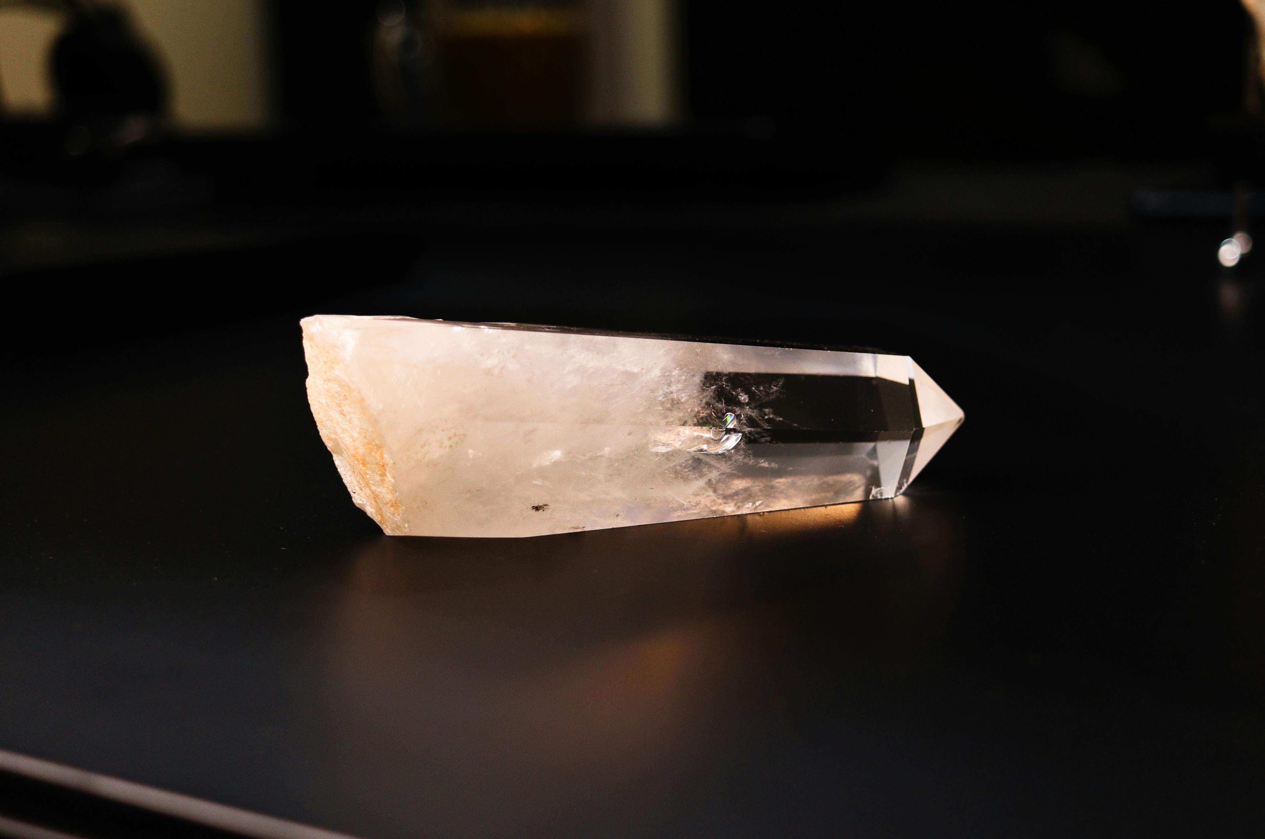 Transparent clear quartz crystal point on dark surface with light reflections