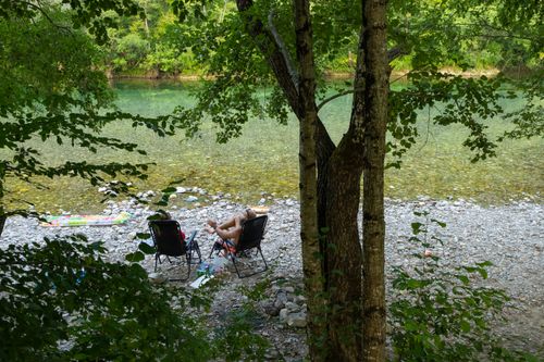 Free Two people relaxing on chairs by a clear riverbank surrounded by lush greenery. Stock Photo