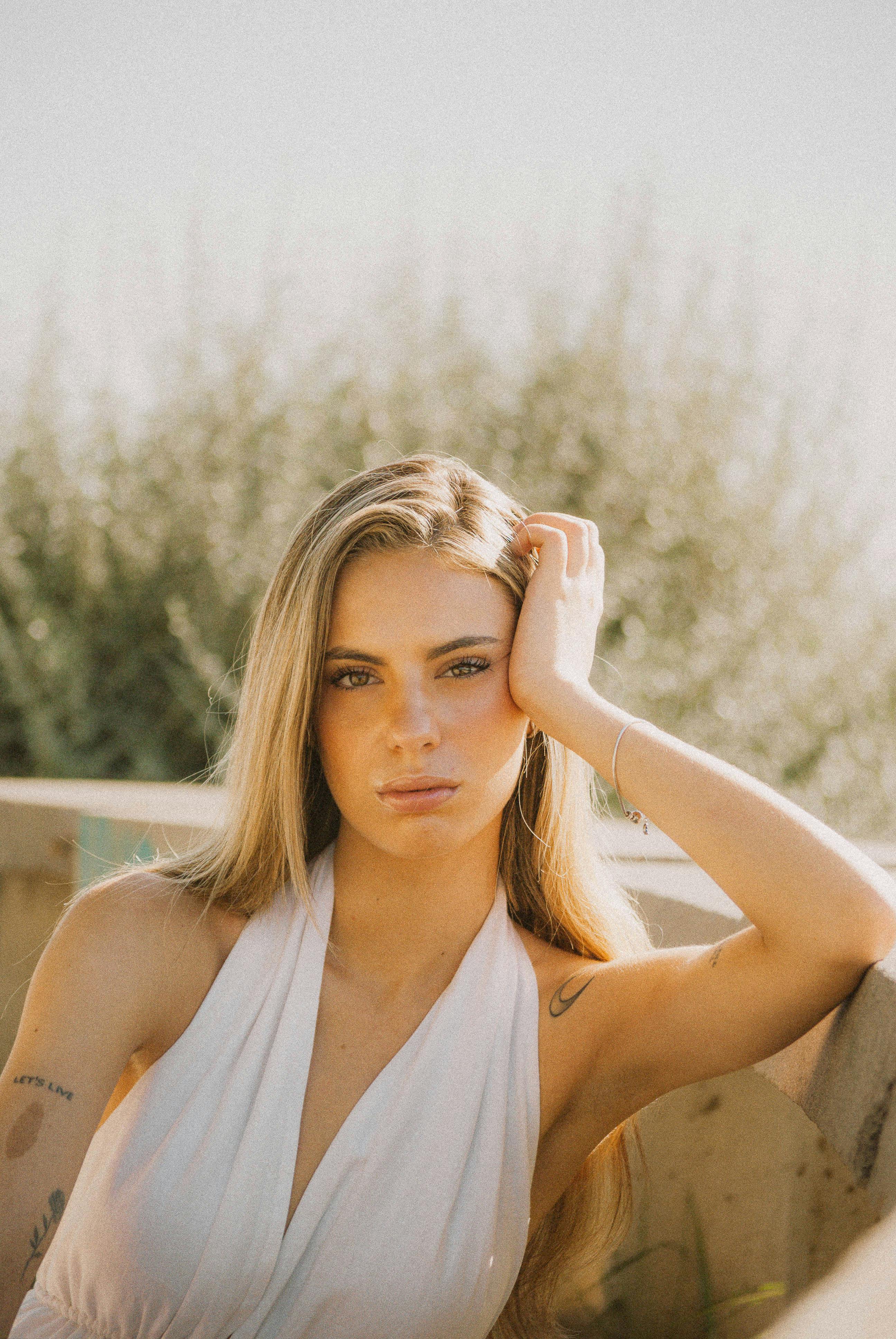 Retrato sereno al aire libre de una mujer joven con un vestido blanco, bañada por la cálida luz del sol.