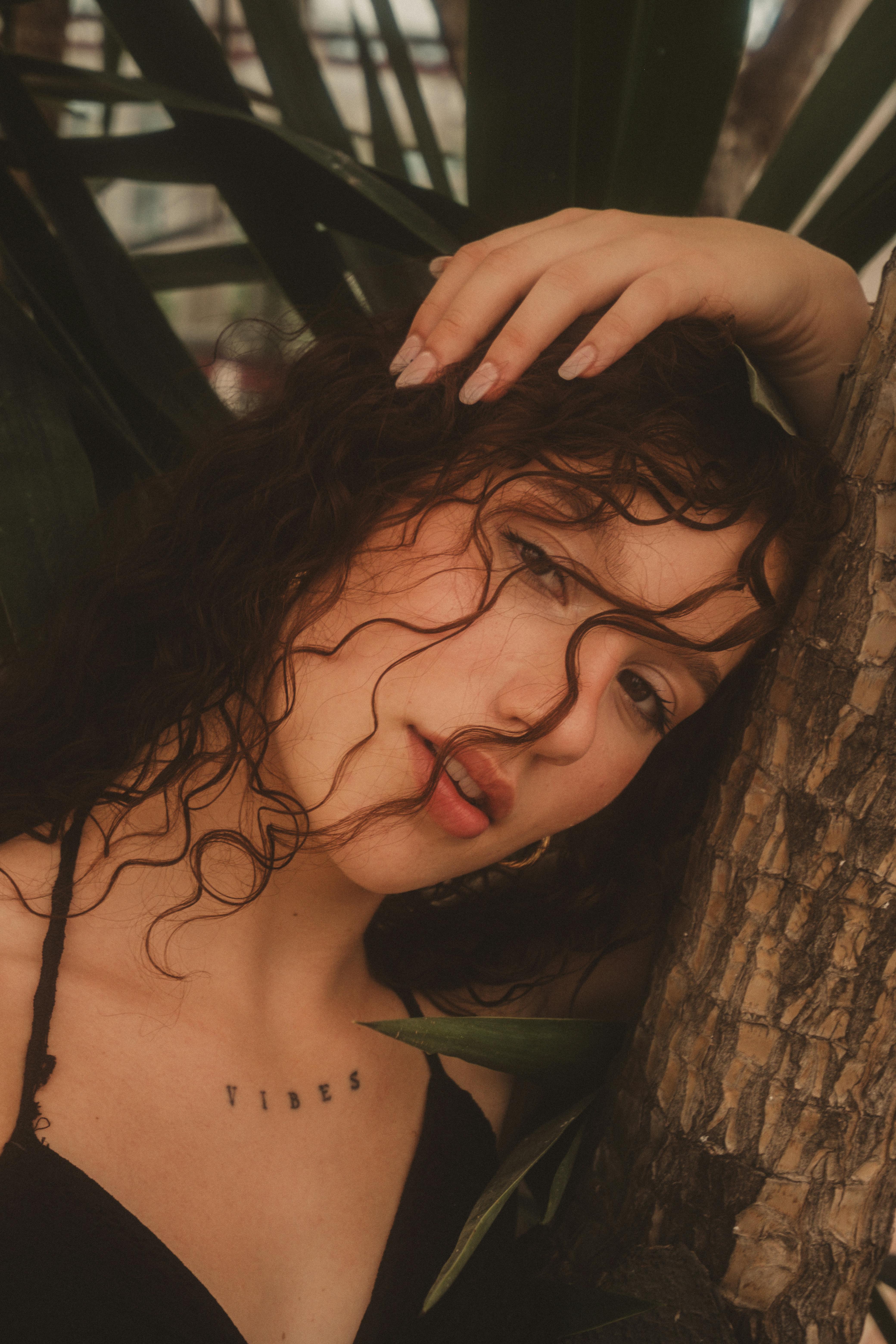 Gratuit Portrait émouvant d'une femme appuyée contre un arbre, baignée d'une lumière tamisée. Photos