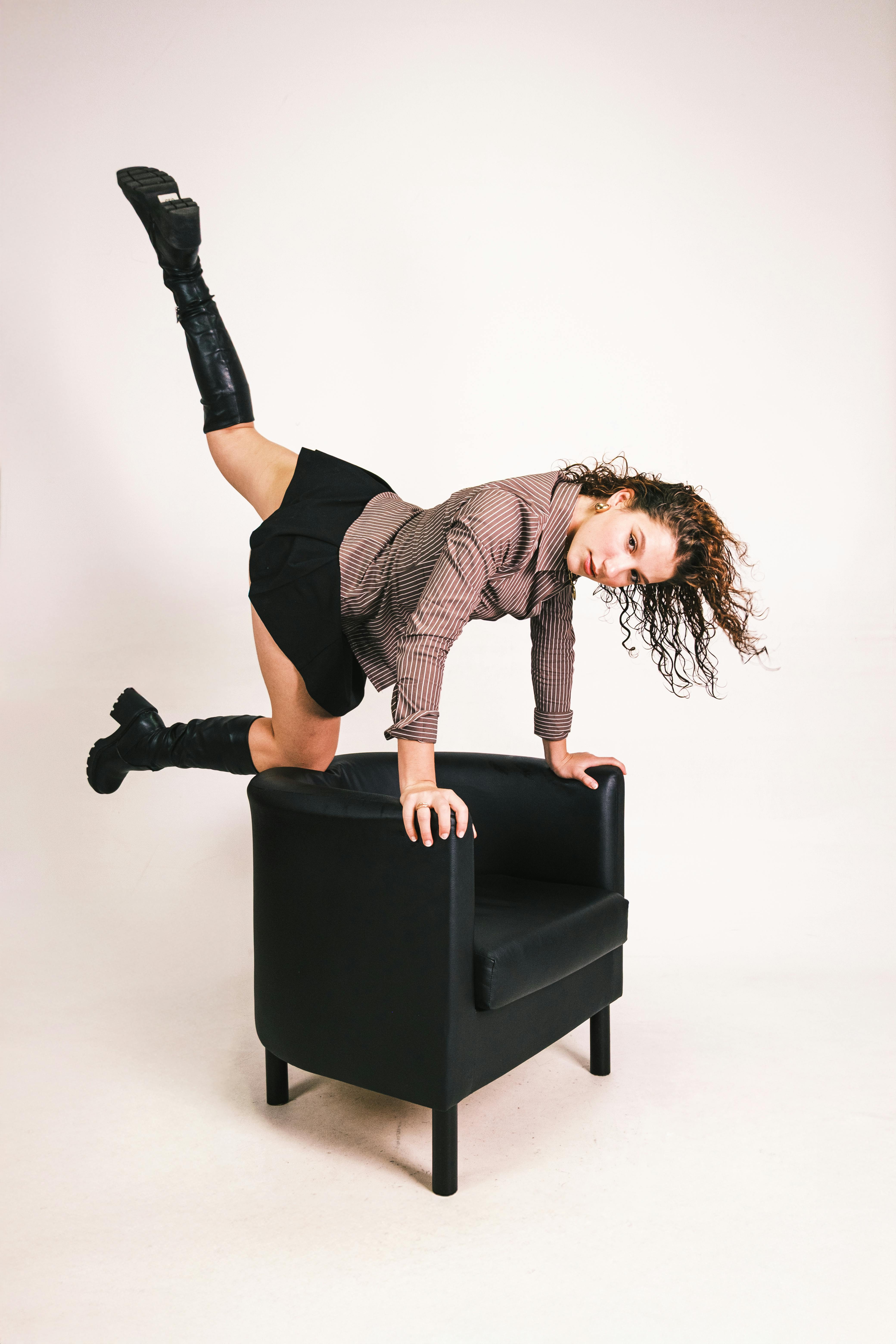 Kostnadsfria Ung kvinna intar en akrobatisk pose på en svart stol i en studio. Stock foto