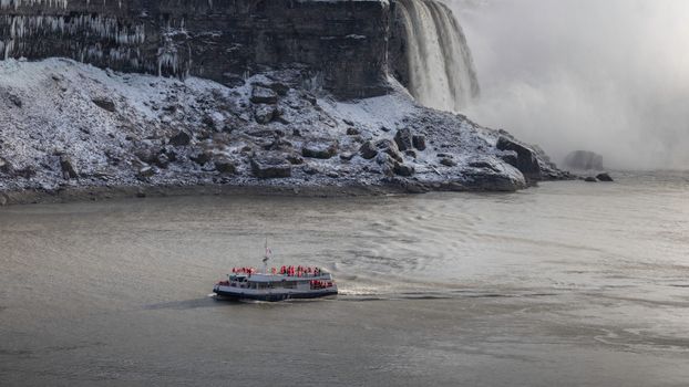 Tour boat navigating near icy Niagara Falls in winter. Stunning view.
