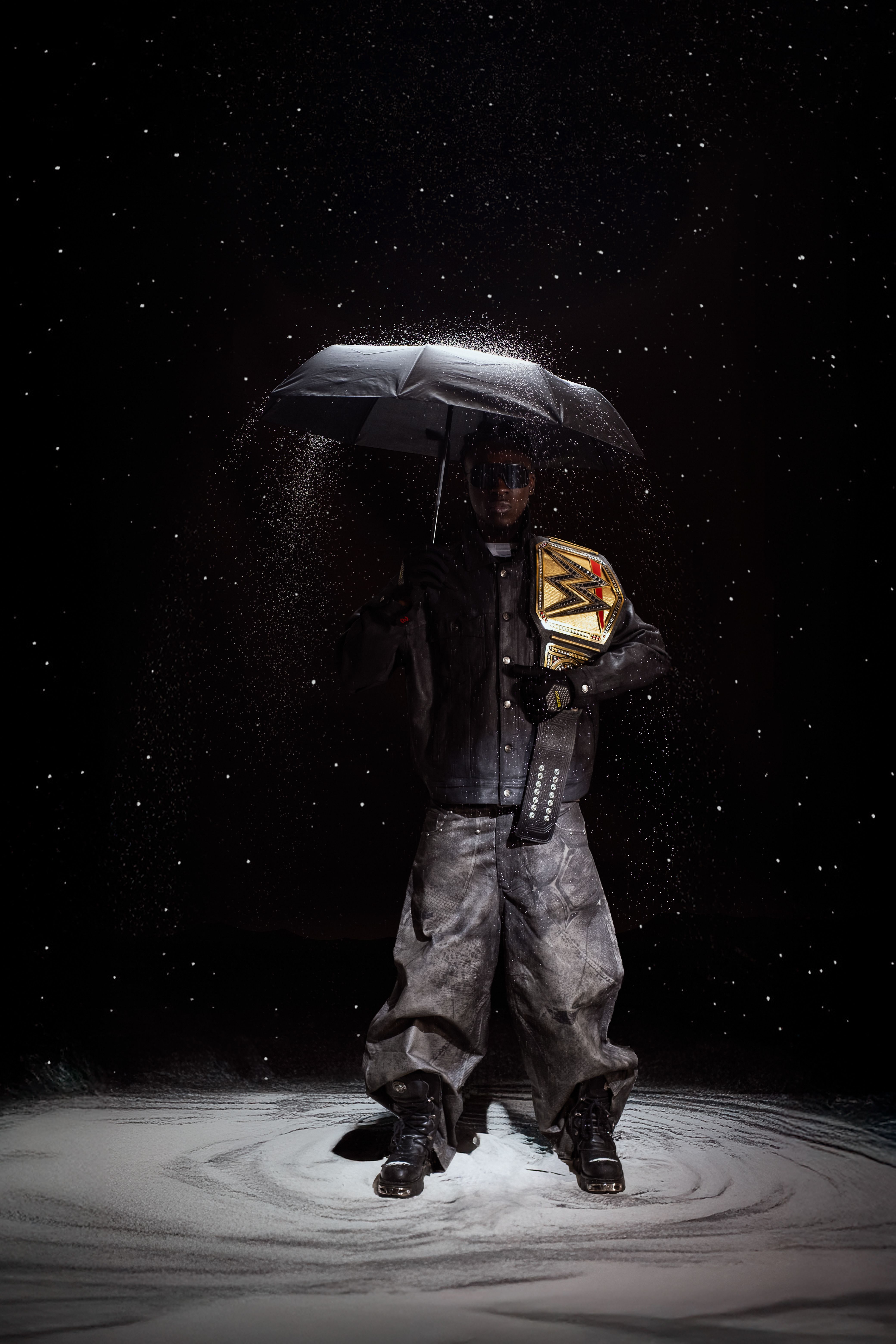 A person holding a championship belt under an umbrella, surrounded by darkness.