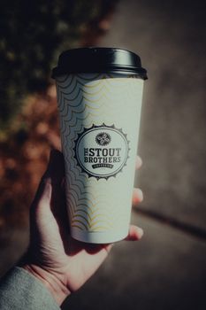 Person holding a Stout Brothers coffee cup outdoors on a sunny day.