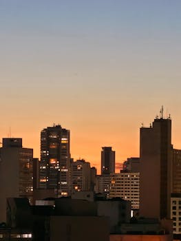 Urban skyline silhouette against a vibrant orange sunset, creating a stunning cityscape scene.