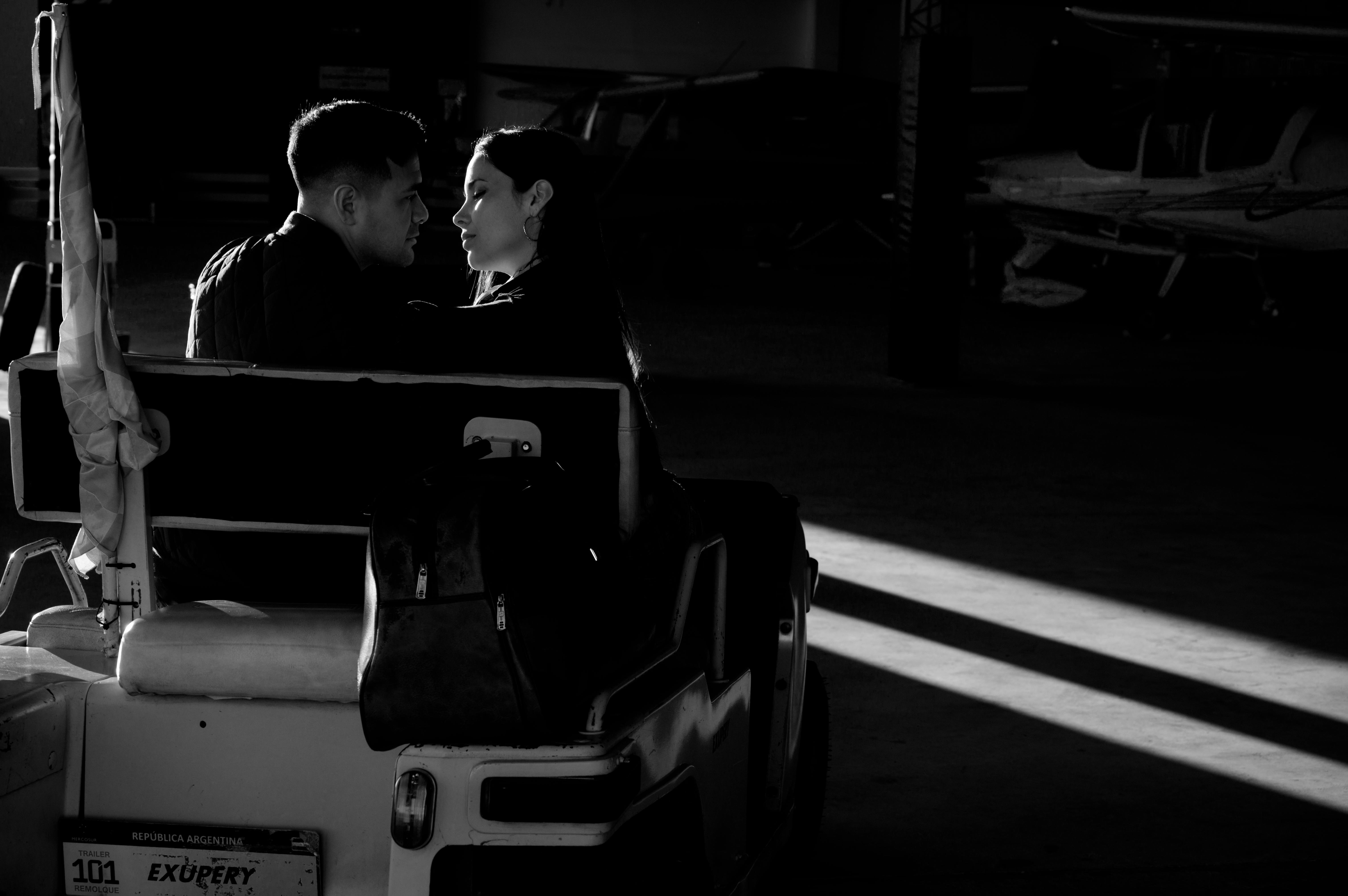 Zadarmo Čiernobiela fotografia páru zdieľajúceho okamih v siluete v hangári lietadla. Fotka z fotobanky