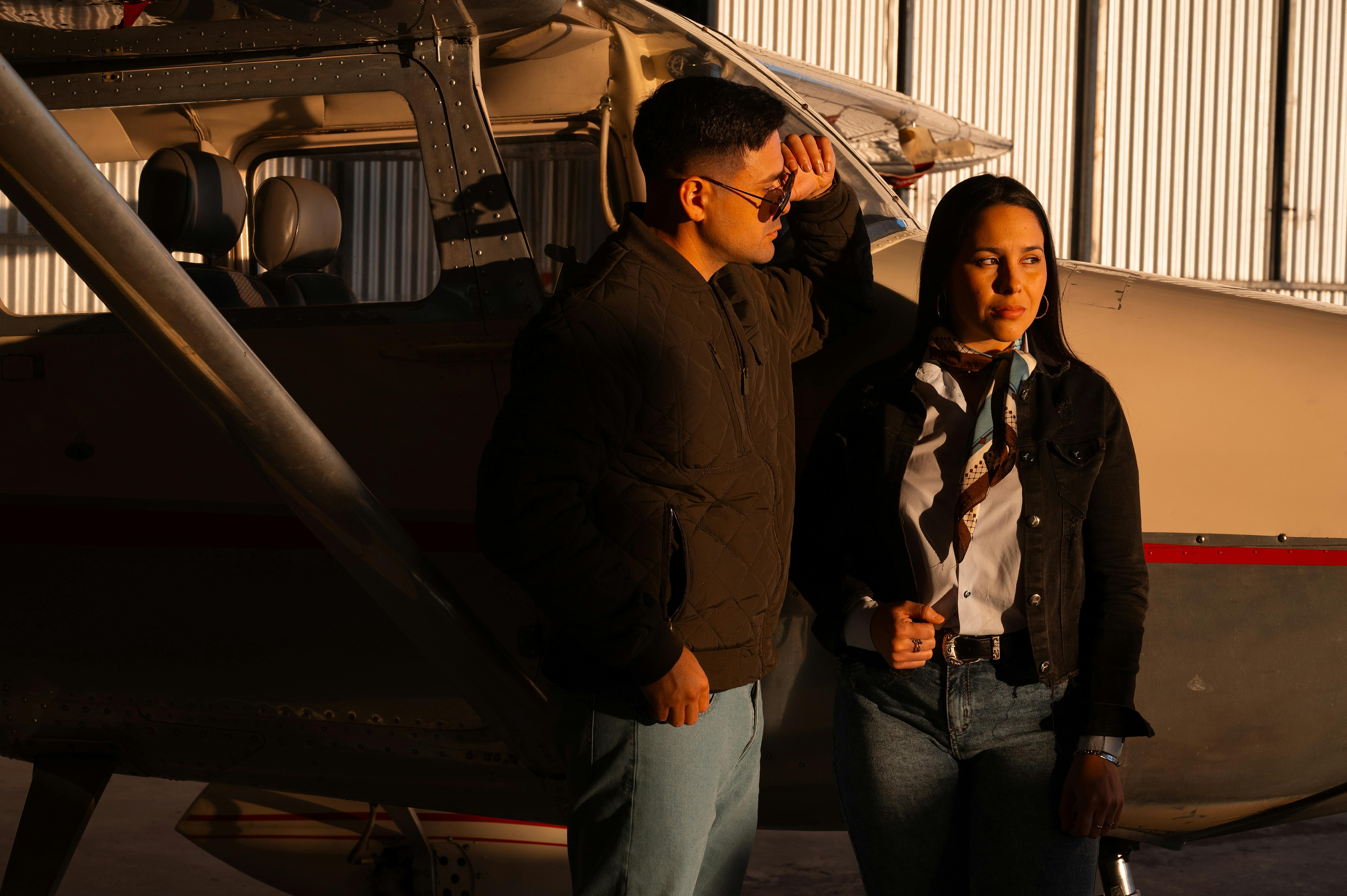 Zadarmo Módny pár pózuje pri lietadle v hangári, pod teplým osvetlením. Fotka z fotobanky