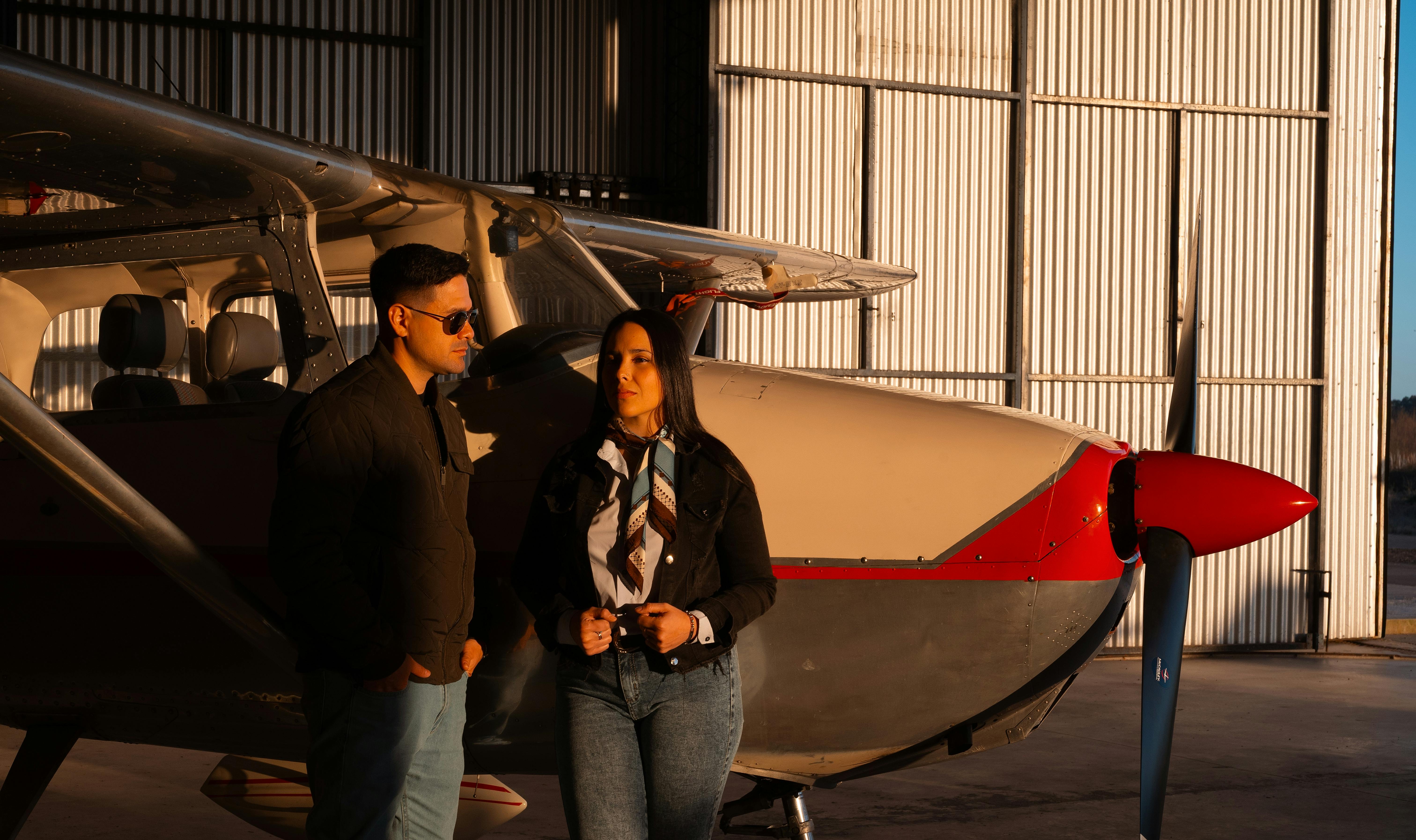 Zadarmo Módny pár stojaci pri malom lietadle v slnkom zaliatom hangári. Fotka z fotobanky