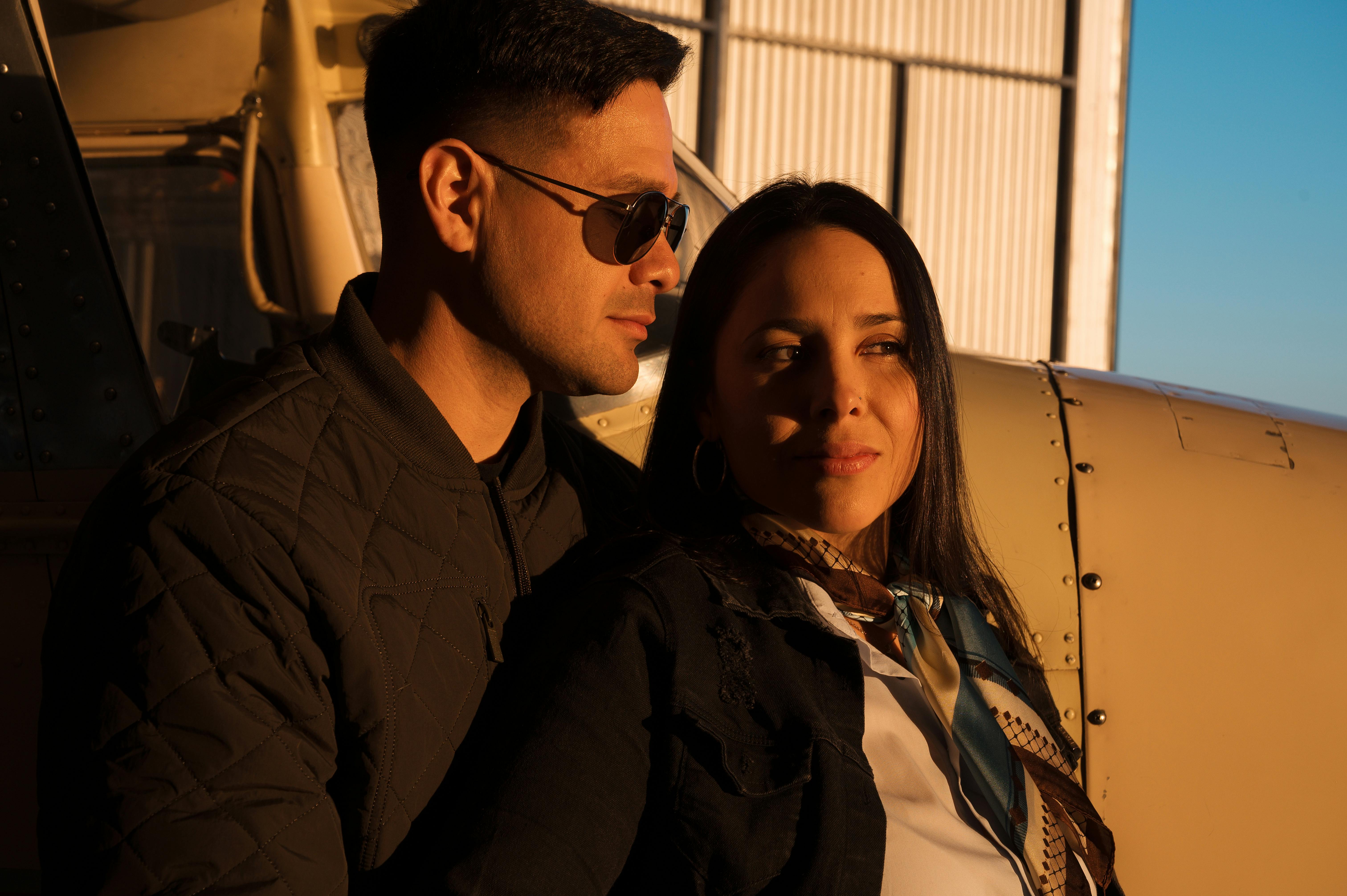 Zadarmo Pár stojaci pri lietadle v hangári počas západu slnka a predstavujúci štýlovú leteckú tému. Fotka z fotobanky