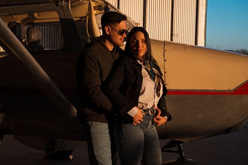 Free A couple embraces warmly beside an airplane inside a hangar during sunset. Stock Photo
