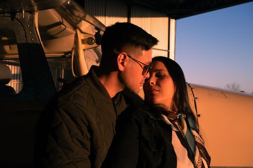 Free A couple shares a tender moment near a private aircraft inside a hangar. Stock Photo