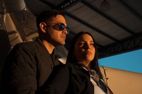 Free Stylish couple posing by an airplane in an industrial hangar setting. Stock Photo