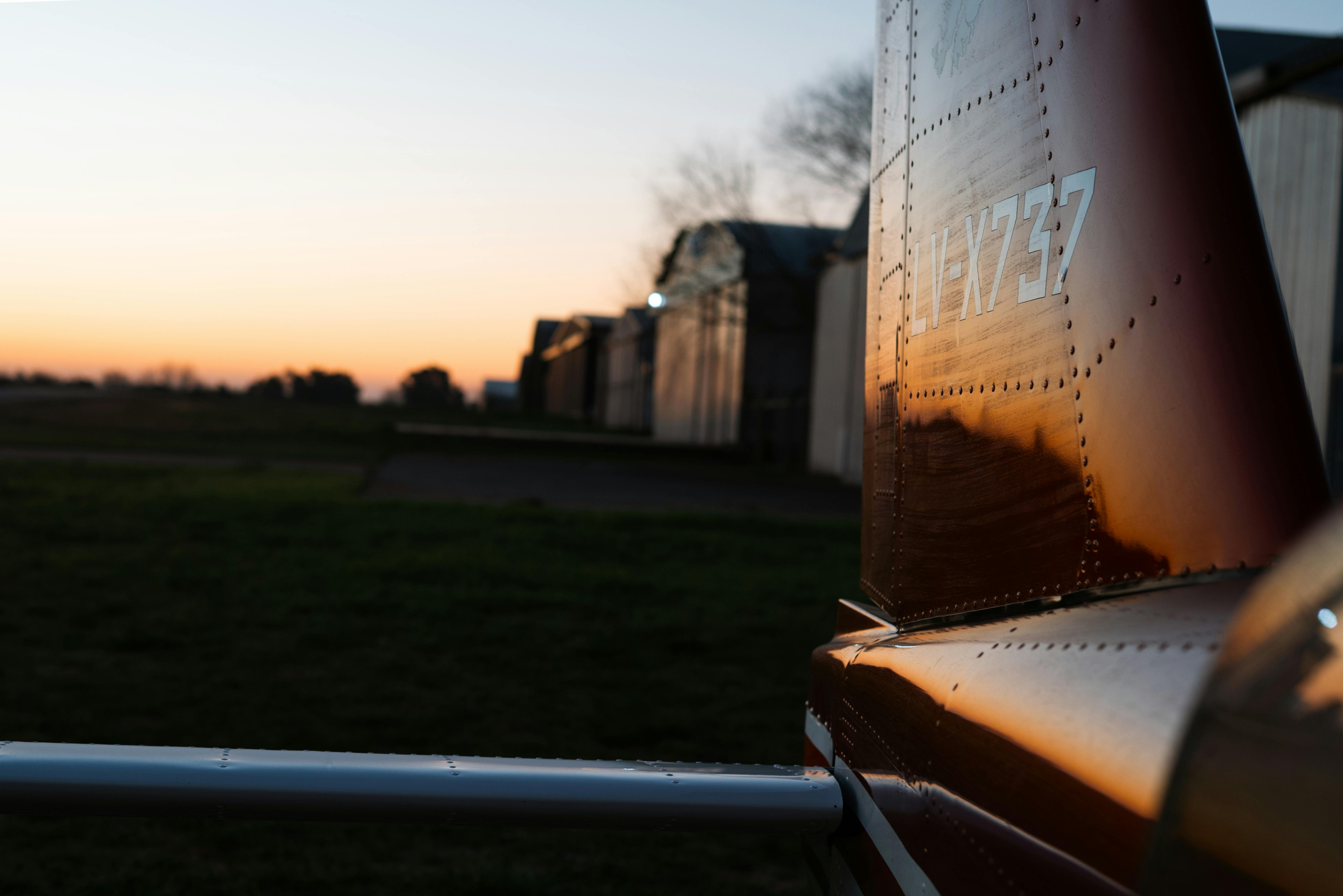 Zadarmo Detailný záber na chvost lietadla odrážajúci odtiene západu slnka pri leteckom hangári. Fotka z fotobanky
